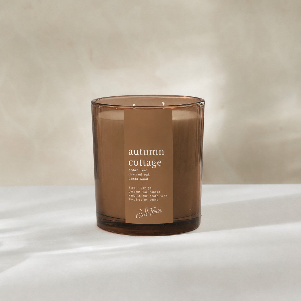 An amber glass jar candle with a brown paper label reading &