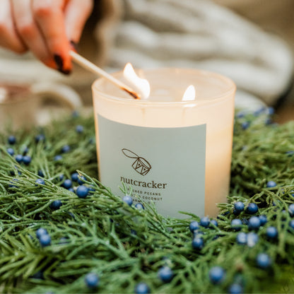 Candle being lit with a match, surrounded by greenery and berries, with &