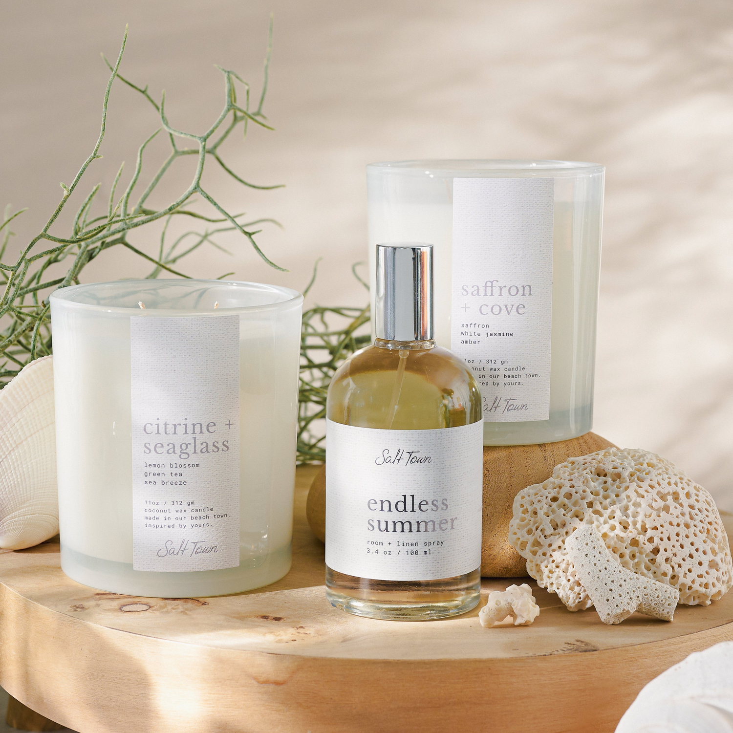 Two candles and a bottle of diffuser on a wooden stand with natural elements.