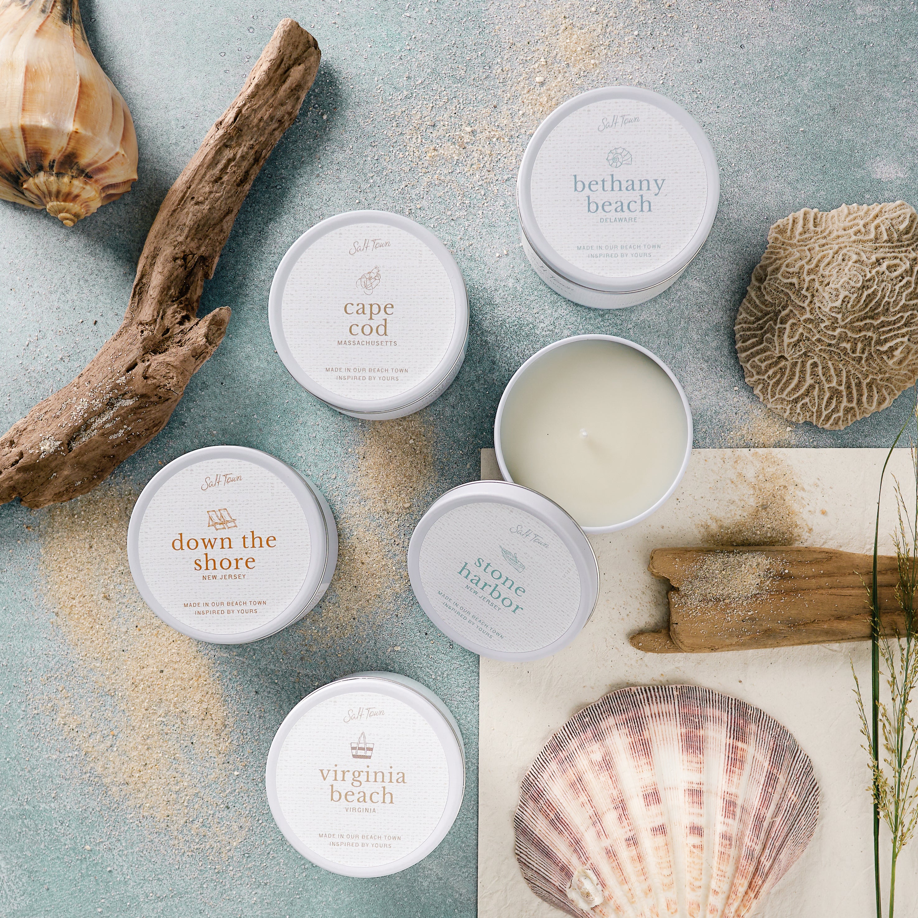 Collection of beach-themed containers with lids on a textured surface with natural elements.