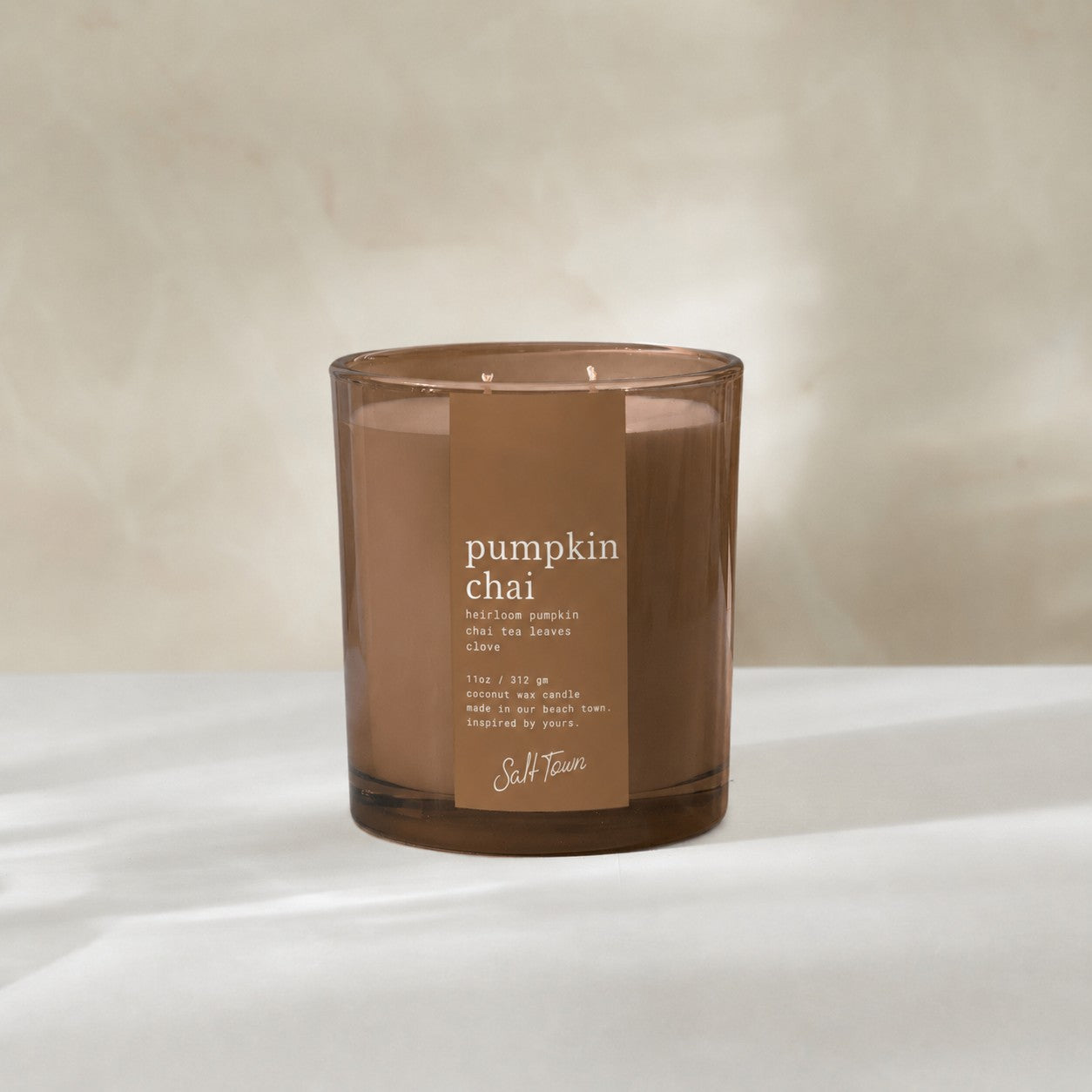 Coco colored glass candle vessel with pumpkin chai on the label. 